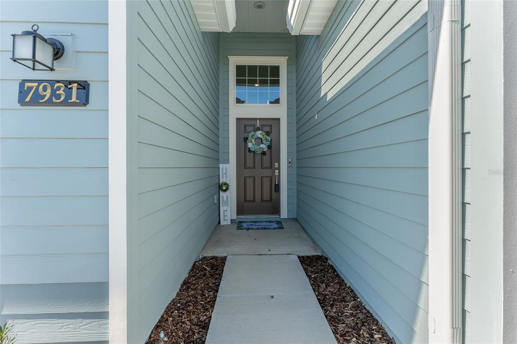 A light blue house exterior features a covered entryway with a brown front door — 7931 SW 74TH LOOP, OCALA, FL