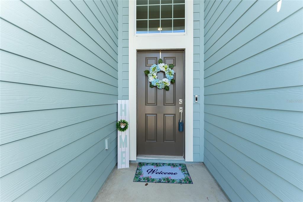A front entryway features light blue horizontal siding, a brown door with a wreath, and a mat — 7931 SW 74TH LOOP, OCALA, FL