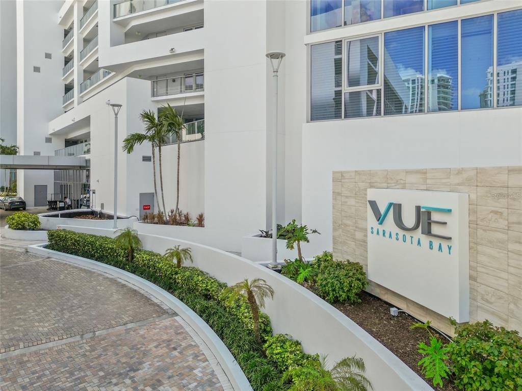 The exterior of a modern white building features a sign reading VUE SARASOTA BAY — 1155 N GULFSTREAM AVENUE UNIT 306, SARASOTA, FL