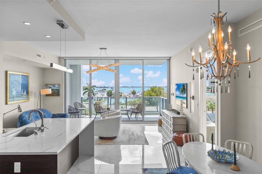A modern open-concept living and dining area features a kitchen island, chandelier, and balcony view — 1155 N GULFSTREAM AVENUE UNIT 306, SARASOTA, FL