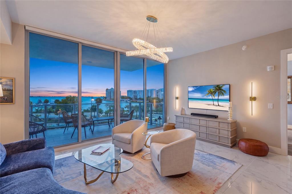 A living room features a glass coffee table, two armchairs, and floor-to-ceiling windows overlooking water — 1155 N GULFSTREAM AVENUE UNIT 306, SARASOTA, FL