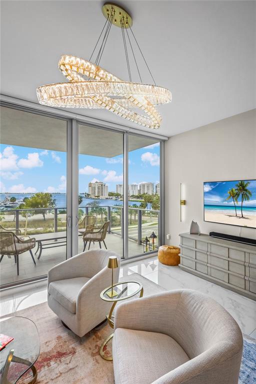 A modern living room features a crystal chandelier, two armchairs, and a balcony overlooking water — 1155 N GULFSTREAM AVENUE UNIT 306, SARASOTA, FL