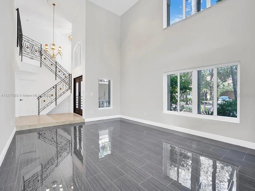 A high-ceilinged living room features gray tile flooring, a wrought-iron staircase, and large windows — 15945 NW 82ND COURT, MIAMI LAKES, FL