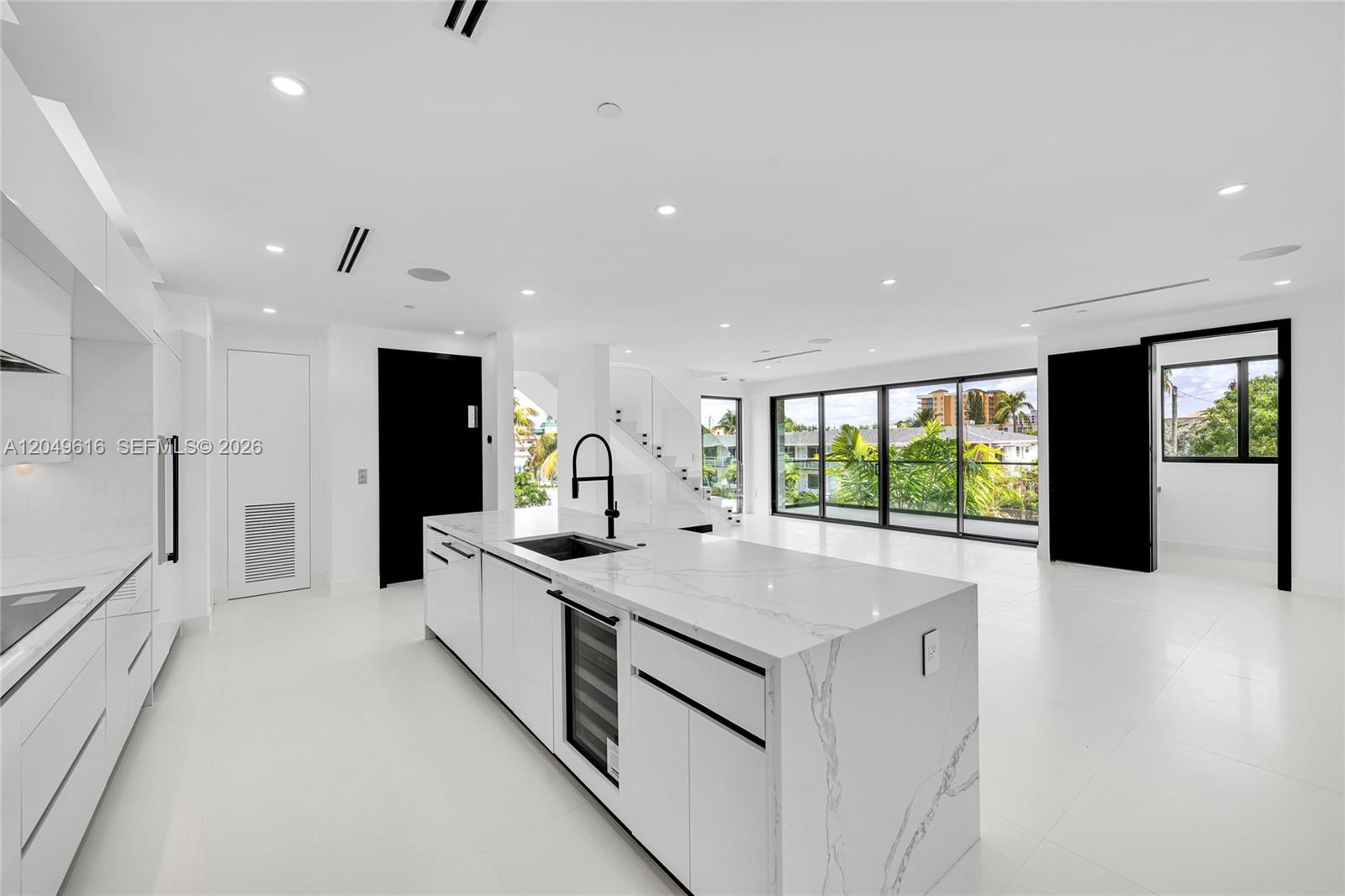 A modern white kitchen features a marble-topped island, black accents, and large glass windows — 3220 NE 7th St, Pompano Beach FL 33062, POMPANO BEACH, FL