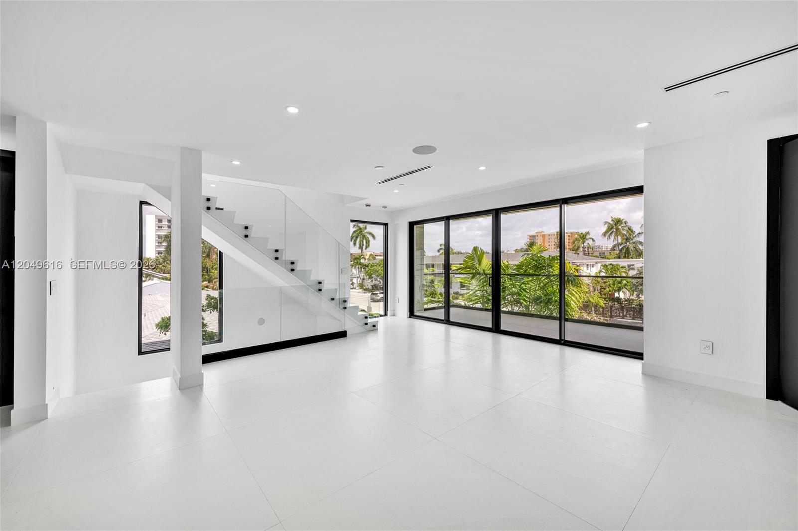 A modern, minimalist living room features white tile floors, a glass-railed staircase, and floor-to-ceiling windows — 3220 NE 7th St, Pompano Beach FL 33062, POMPANO BEACH, FL