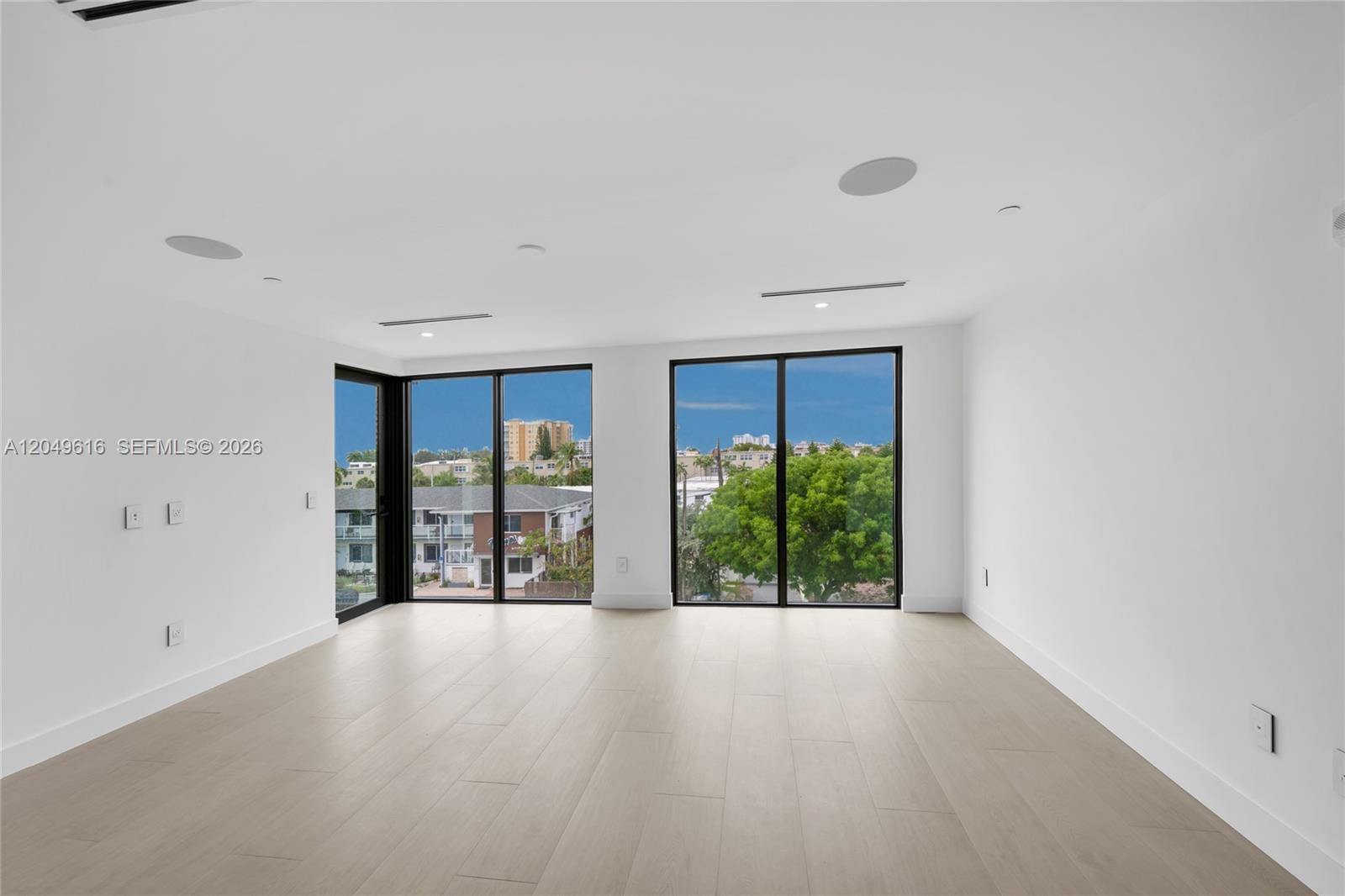 A bright, empty room features white walls, light wood flooring, and large floor-to-ceiling windows — 3220 NE 7th St, Pompano Beach FL 33062, POMPANO BEACH, FL