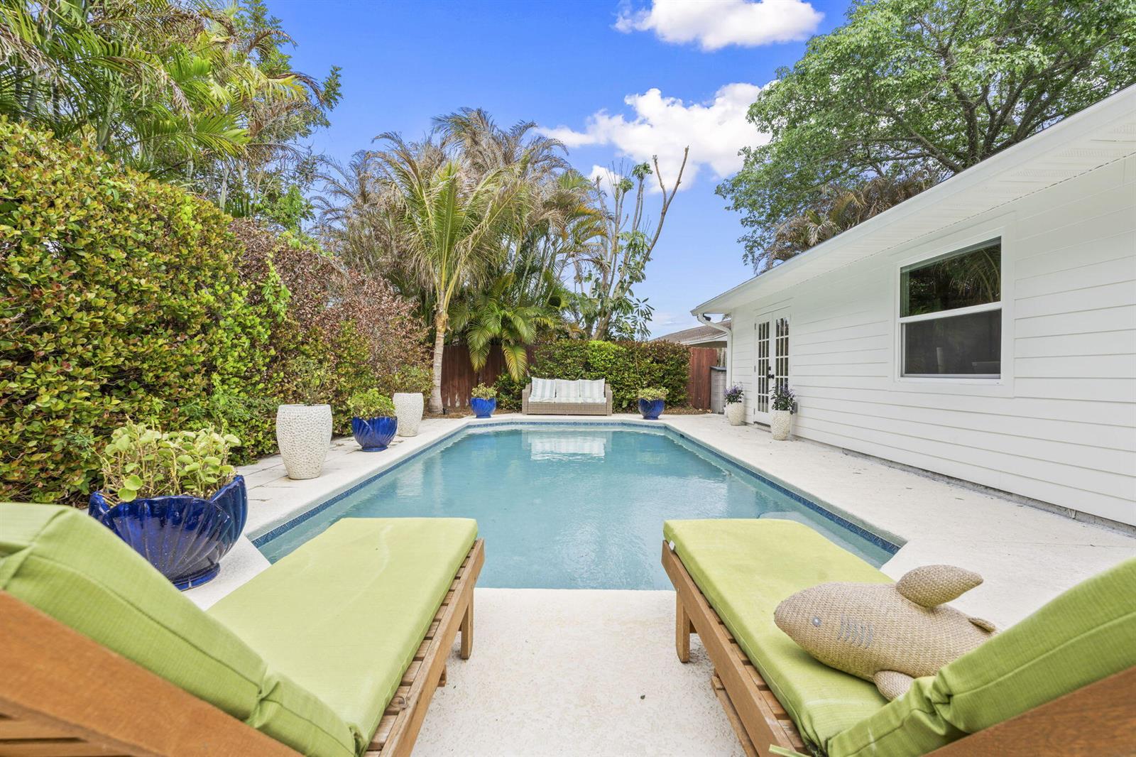 A swimming pool sits in a backyard patio area with lounge chairs and white siding — 1904 NE Avenida Dracaena, Jensen Beach FL 34957, JENSEN BEACH, FL