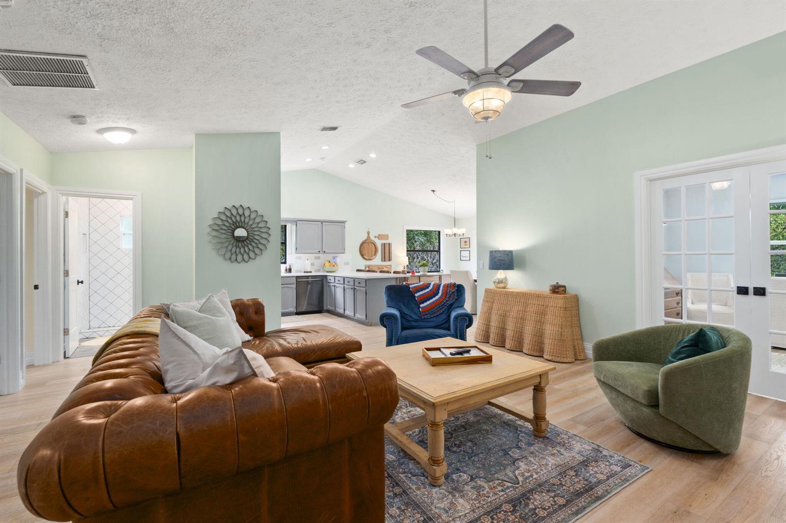 A living room with a leather sofa, blue armchair, green swivel chair, and kitchen beyond — 1904 NE Avenida Dracaena, Jensen Beach FL 34957, JENSEN BEACH, FL