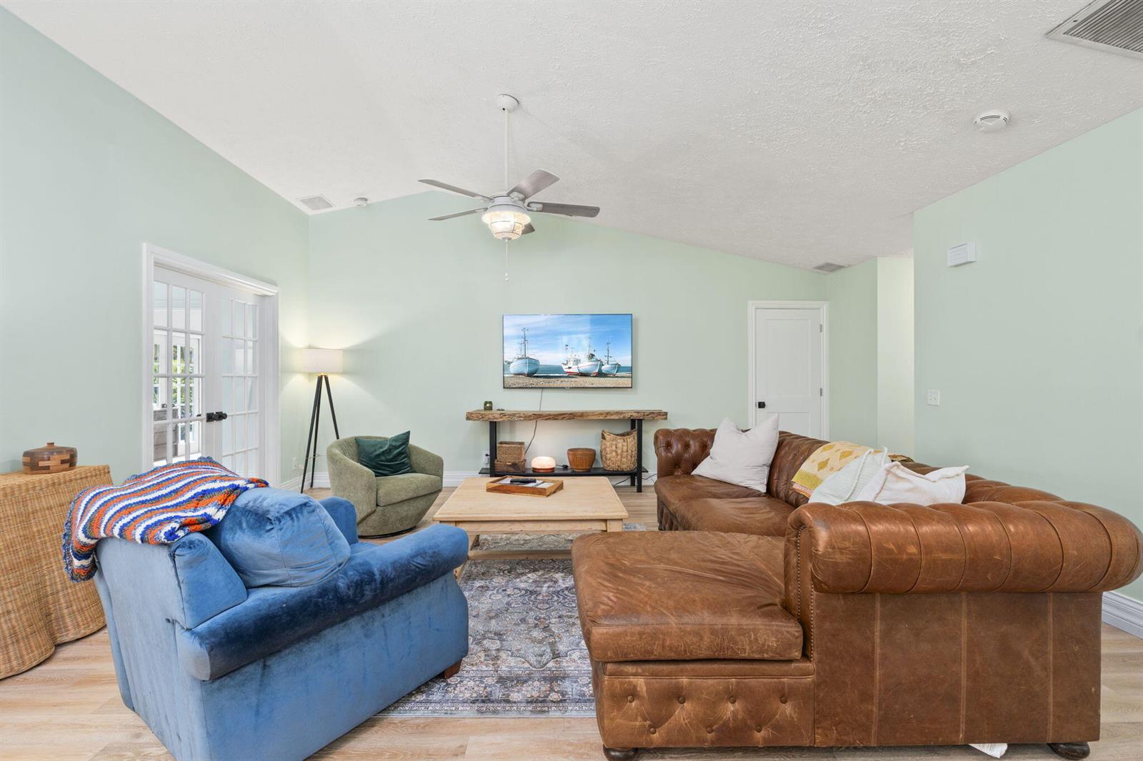 A living room features a leather sectional, blue armchair, light wood coffee table, and television — 1904 NE Avenida Dracaena, Jensen Beach FL 34957, JENSEN BEACH, FL