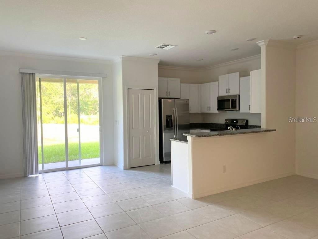 A kitchen with white cabinets and granite countertops opens to a tiled living area — 17478 NECTAR FLUME DRIVE, LAND O LAKES, FL