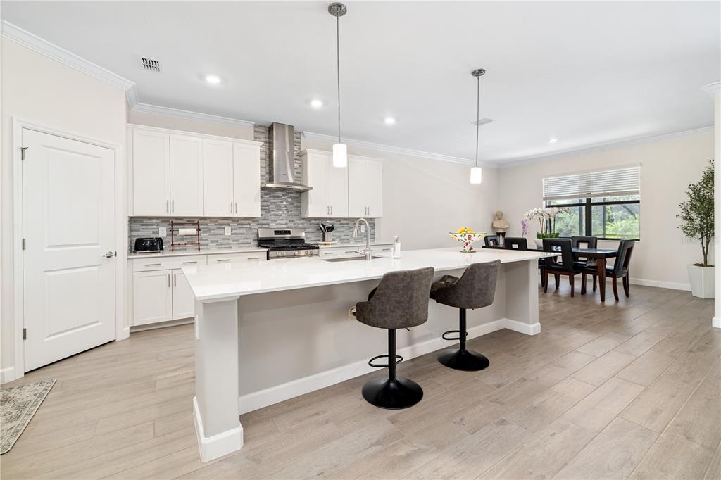 A modern kitchen features white cabinetry, a large quartz island with bar stools, and tile flooring — 5030 SARATOGA SPRINGS RUN, BRADENTON, FL