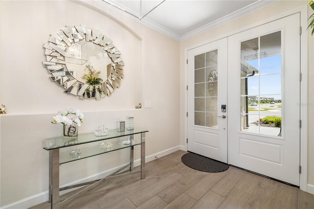 An entryway features a glass console table, a decorative sunburst mirror, and double glass-paneled doors — 5030 SARATOGA SPRINGS RUN, BRADENTON, FL