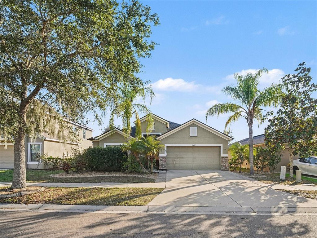 A single-story house with a beige stucco exterior, a two-car garage, and palm trees — 11409 FLORA SPRINGS DRIVE, RIVERVIEW, FL
