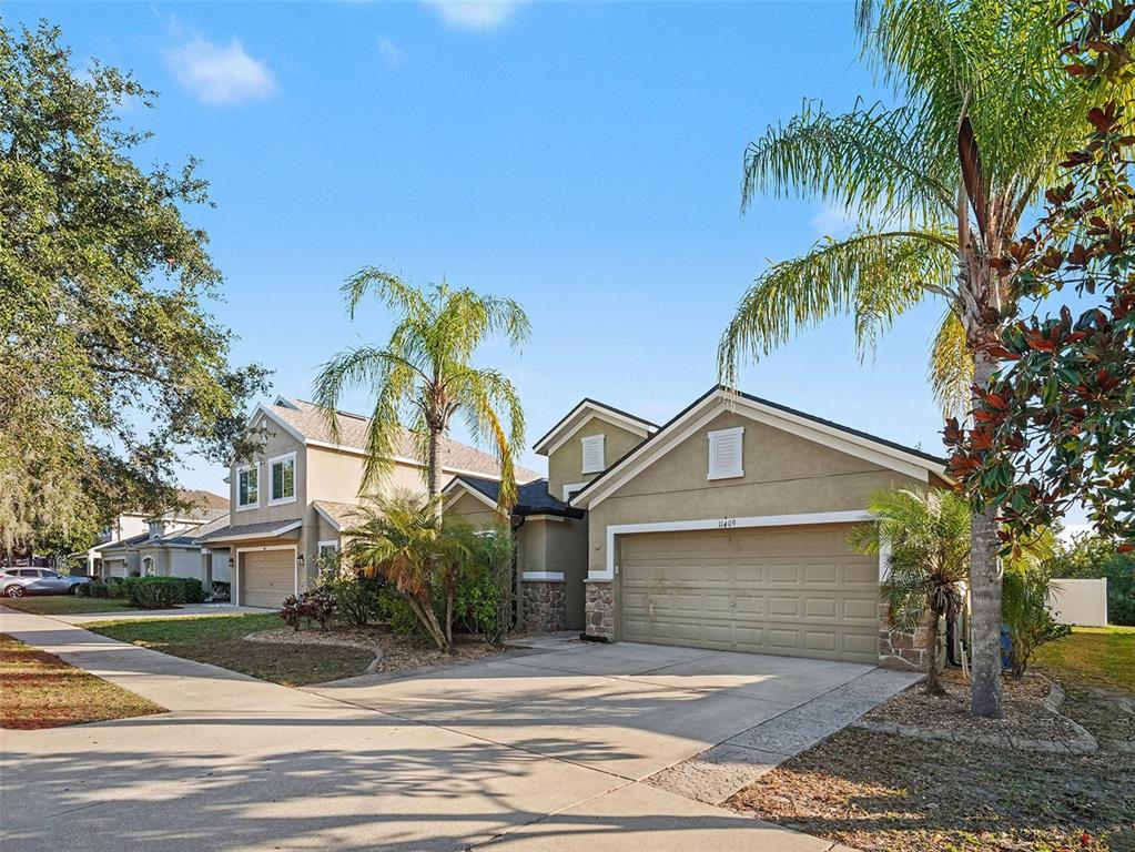 A tan, single-story suburban house with a two-car garage and palm trees in the front — 11409 FLORA SPRINGS DRIVE, RIVERVIEW, FL