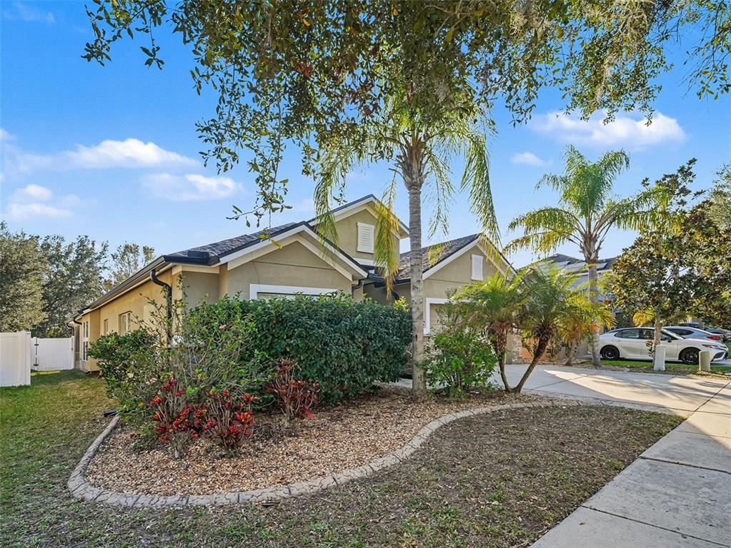 A tan single-story house with a landscaped front yard, palm trees, and a concrete driveway — 11409 FLORA SPRINGS DRIVE, RIVERVIEW, FL