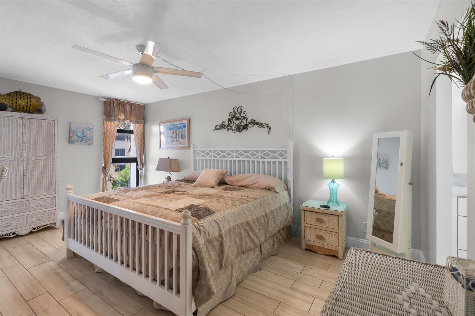A bedroom features a white bed frame, wicker furniture, light wood-look flooring, and a ceiling fan — 1361 S Ocean Boulevard # 303, Pompano Beach FL 33062, POMPANO BEACH, FL
