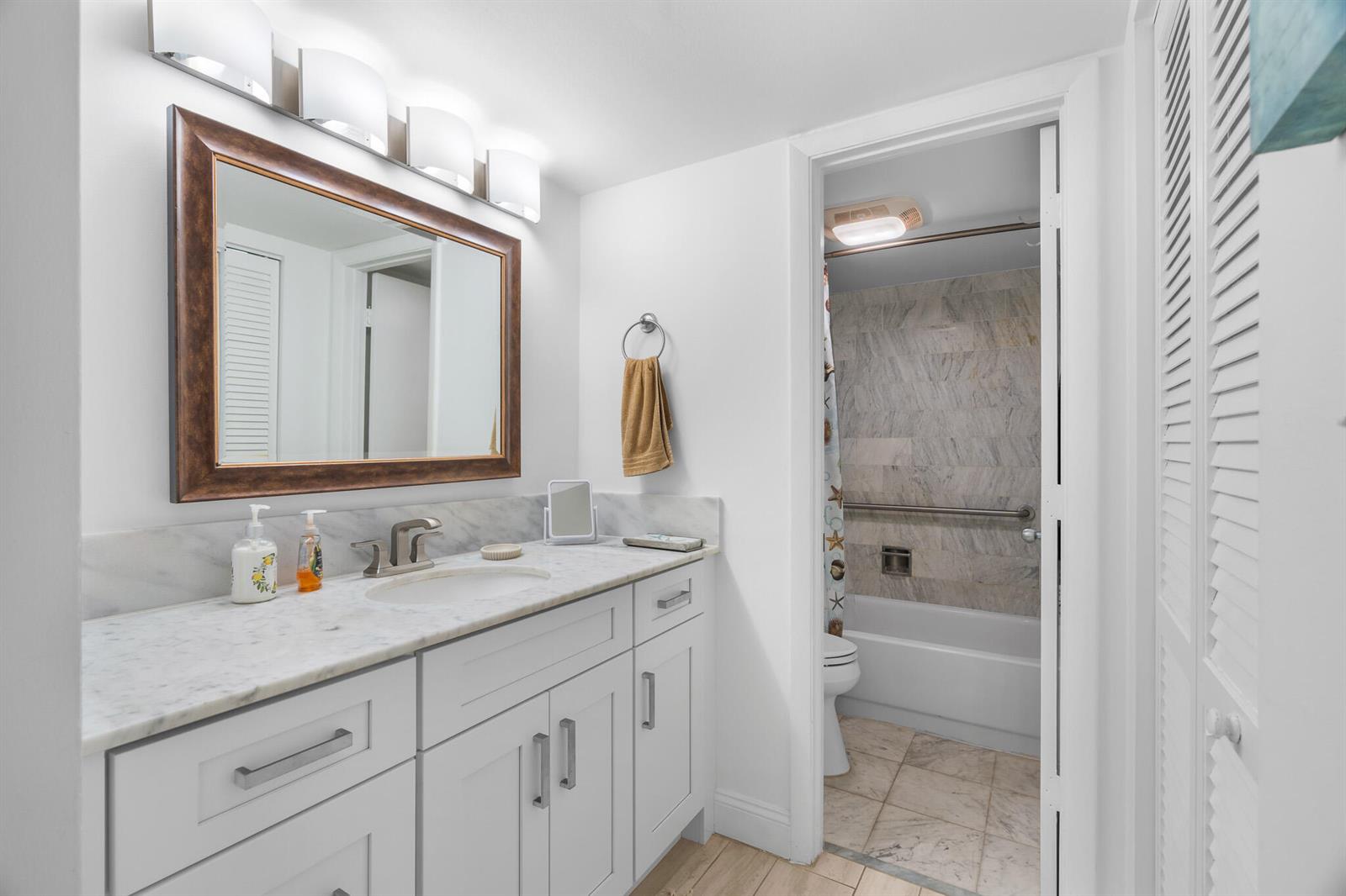 A bathroom features a white vanity with a marble countertop, a framed mirror, and a tub-shower — 1361 S Ocean Boulevard # 303, Pompano Beach FL 33062, POMPANO BEACH, FL