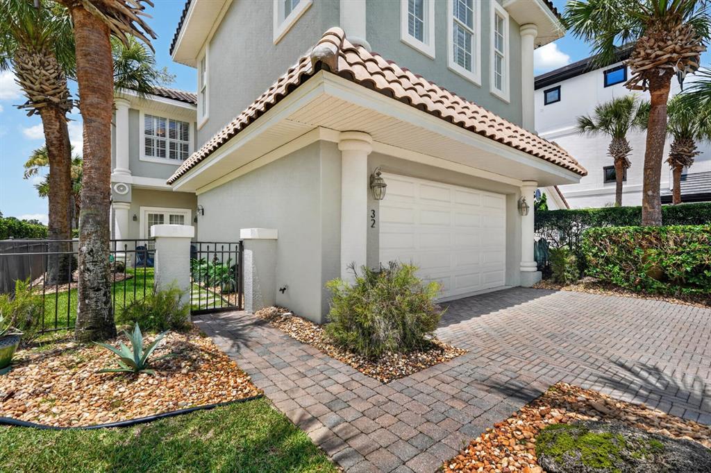 A two-story house exterior features a white garage door, brick paver driveway, and palm trees — 32 NORTHSHORE AVENUE, PALM COAST, FL