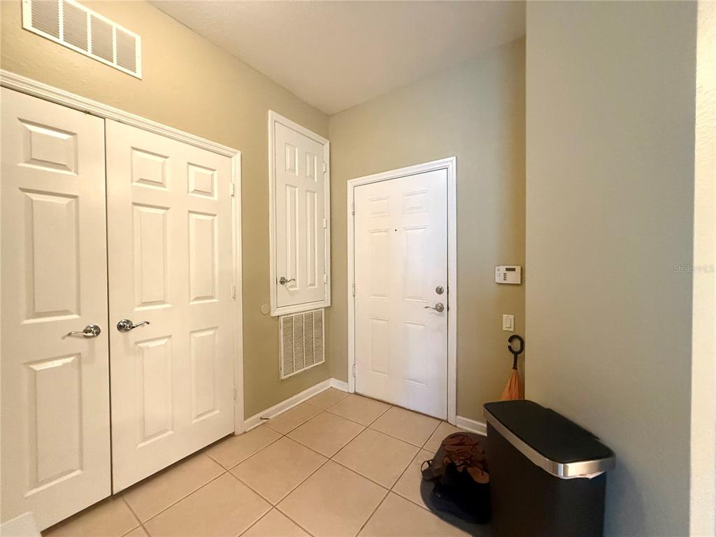 An entryway features tiled flooring, white doors, a wall-mounted thermostat, and a trash can — 3314 ROBERT TRENT JONES DRIVE UNIT 410, ORLANDO, FL