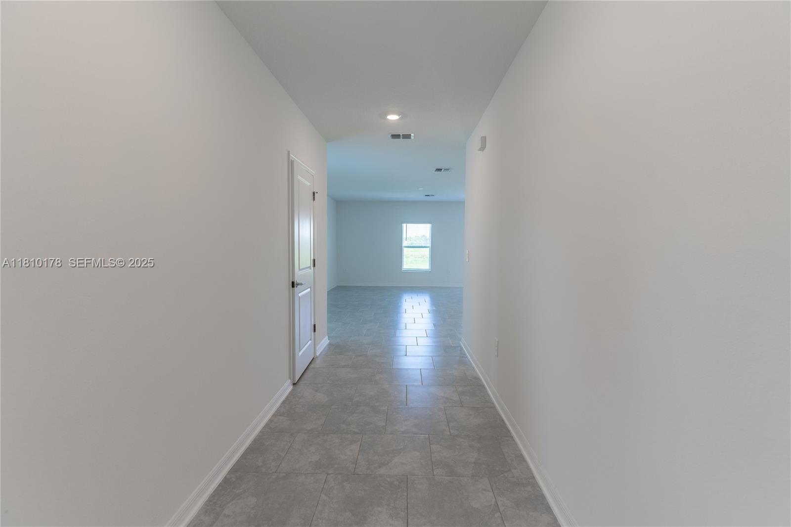 A hallway with gray tile flooring leads to an open room with a window — 934 CATTLEMAN STREET, Winter Haven FL 33884, WINTER HAVEN, FL