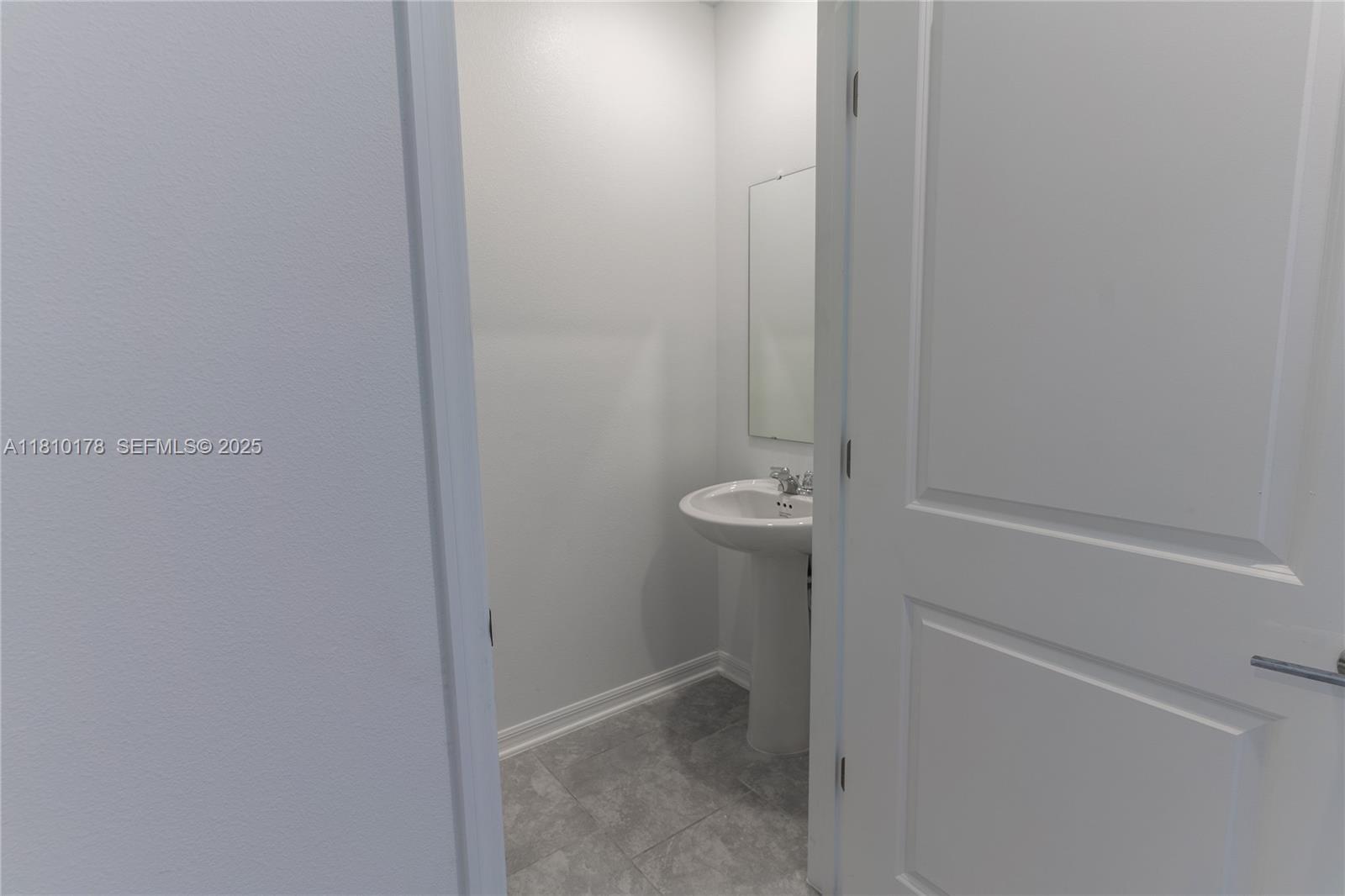 A small bathroom features a white pedestal sink, a wall mirror, and gray tiled flooring — 934 CATTLEMAN STREET, Winter Haven FL 33884, WINTER HAVEN, FL