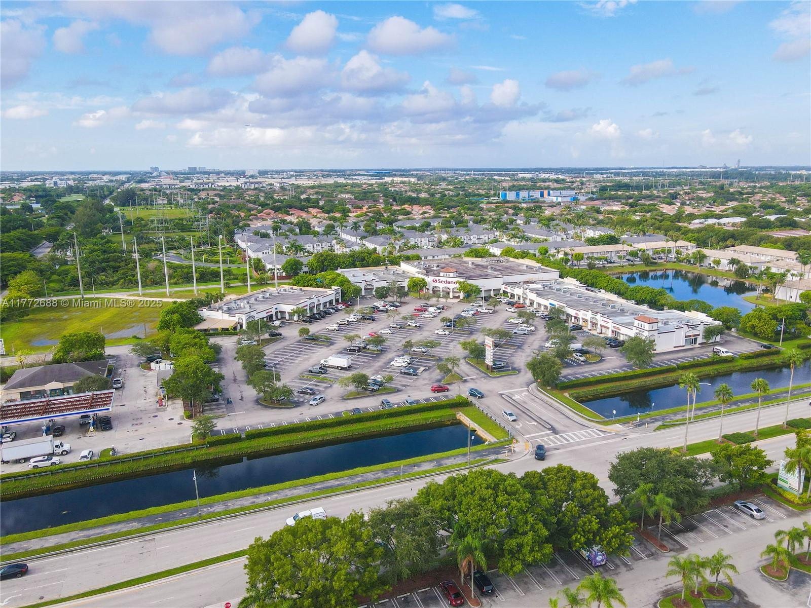 An aerial view shows a commercial shopping center with a large parking lot and canal — 10750 NW 58th St, Doral FL 33178, DORAL, FL