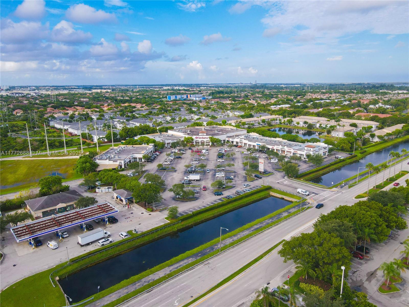 An aerial view shows a shopping plaza with a gas station, parking lot, and canal — 10750 NW 58th St, Doral FL 33178, DORAL, FL