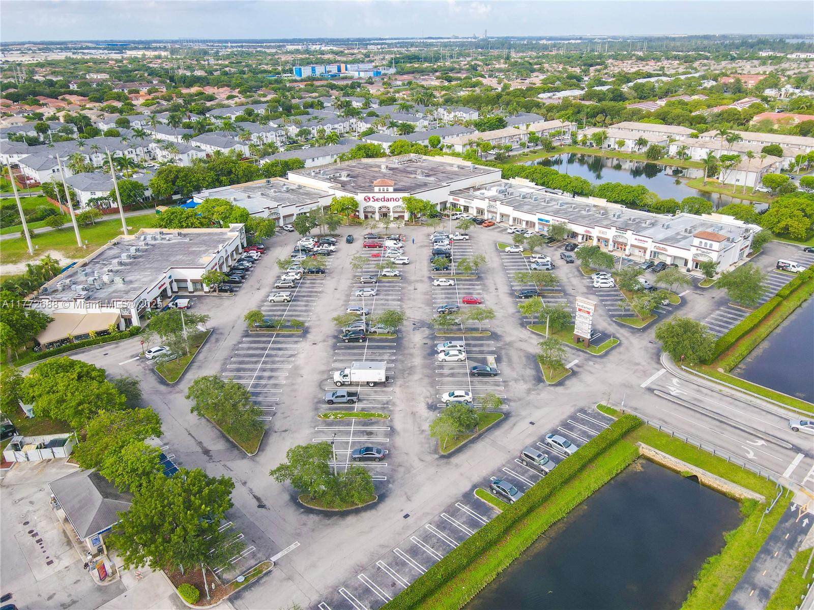 An aerial view shows a commercial shopping center with a large parking lot and ponds — 10750 NW 58th St, Doral FL 33178, DORAL, FL