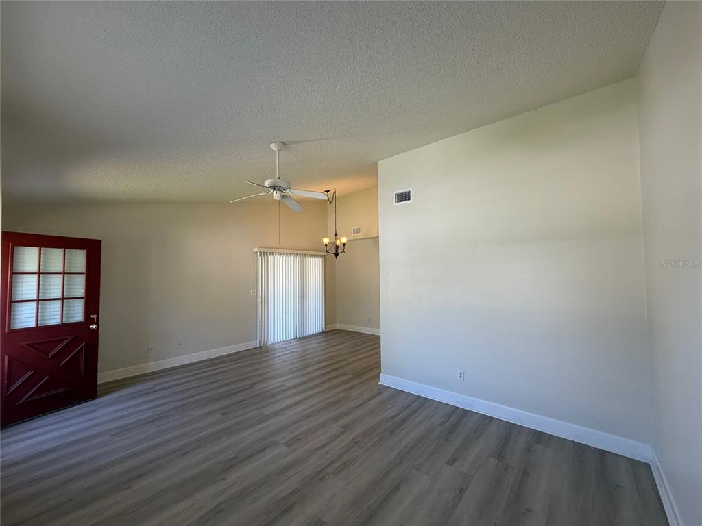 An empty living room features light-colored walls, wood-look flooring, a ceiling fan, and a door — 14 BIRDIE DRIVE, NEW SMYRNA BEACH, FL