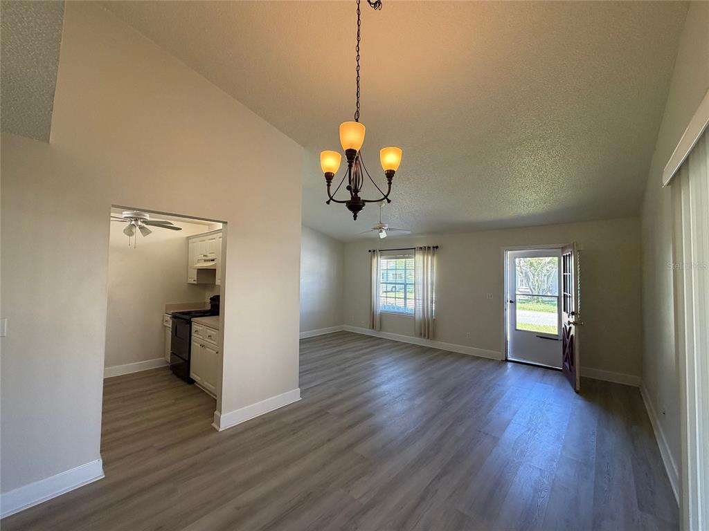 A living room with light wood-look flooring, a chandelier, and an adjacent kitchen — 14 BIRDIE DRIVE, NEW SMYRNA BEACH, FL