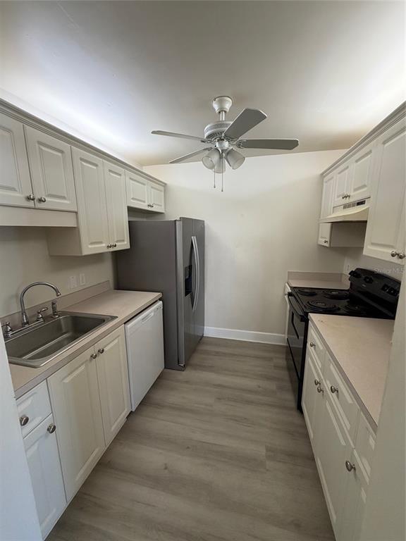 A galley kitchen features white cabinets, stainless steel appliances, and light wood-look flooring — 14 BIRDIE DRIVE, NEW SMYRNA BEACH, FL