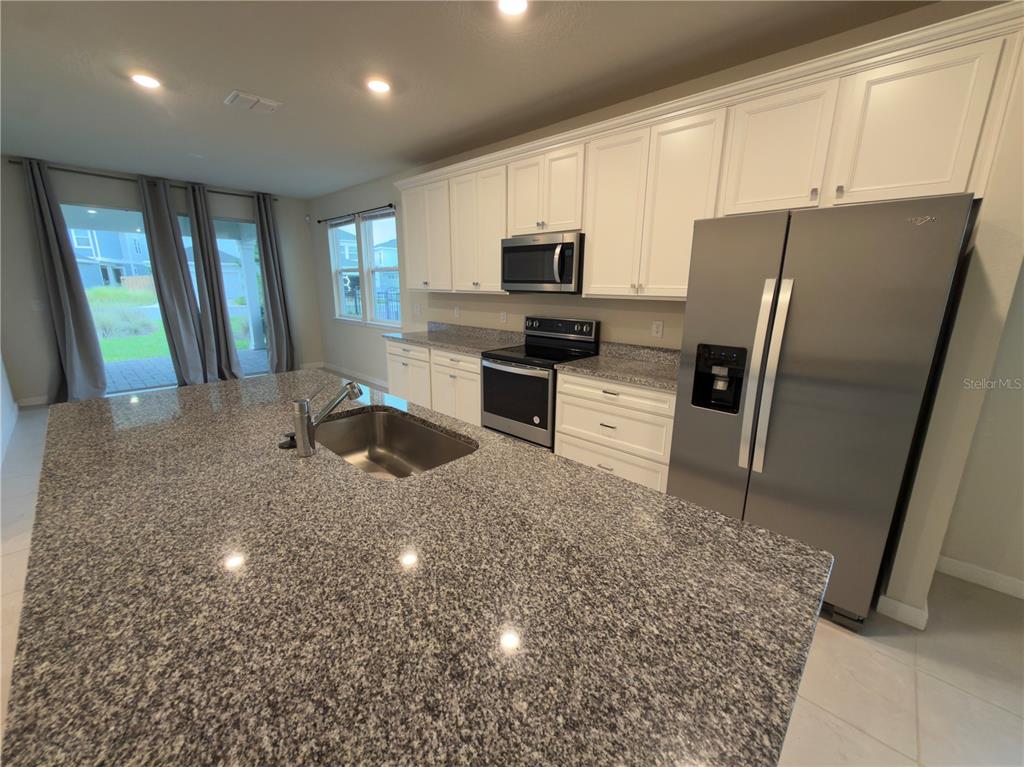 A kitchen features white cabinets, granite countertops, a stainless steel refrigerator, and a center island — 6383 TRAILBLAZE BEND, ST CLOUD, FL
