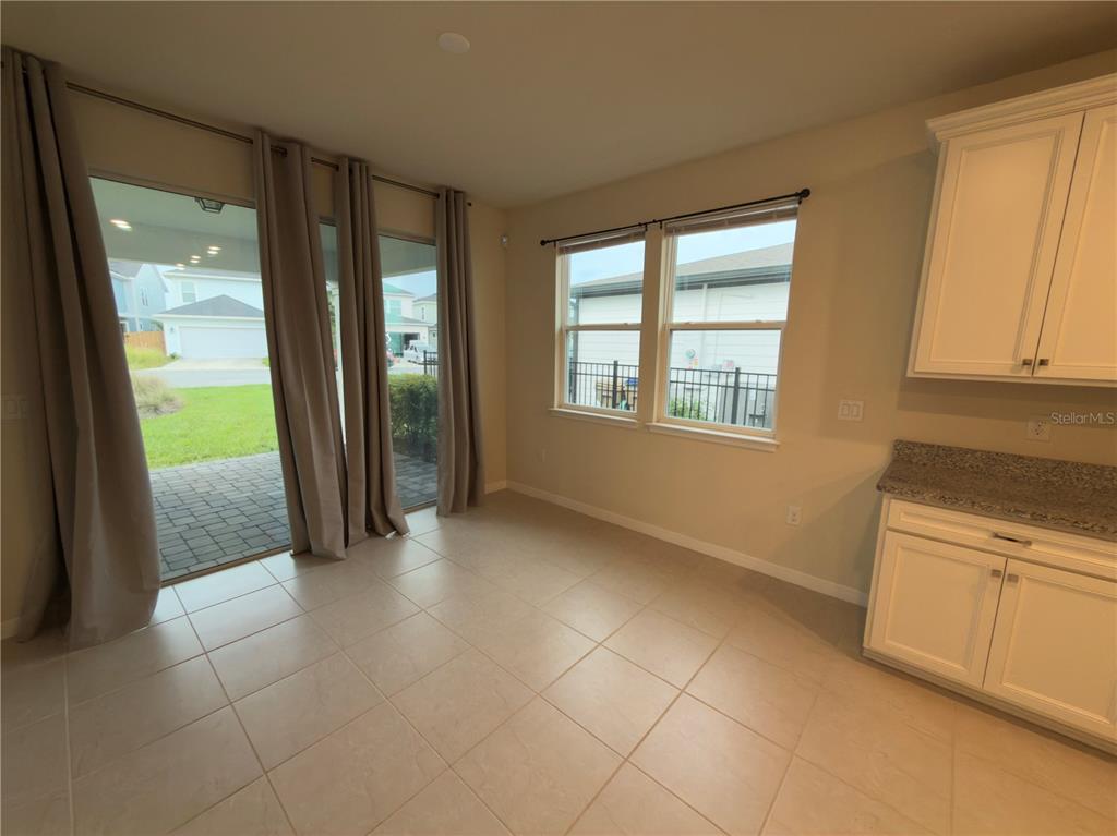 A dining area features tile flooring, sliding glass doors, two windows, and white kitchen cabinets — 6383 TRAILBLAZE BEND, ST CLOUD, FL