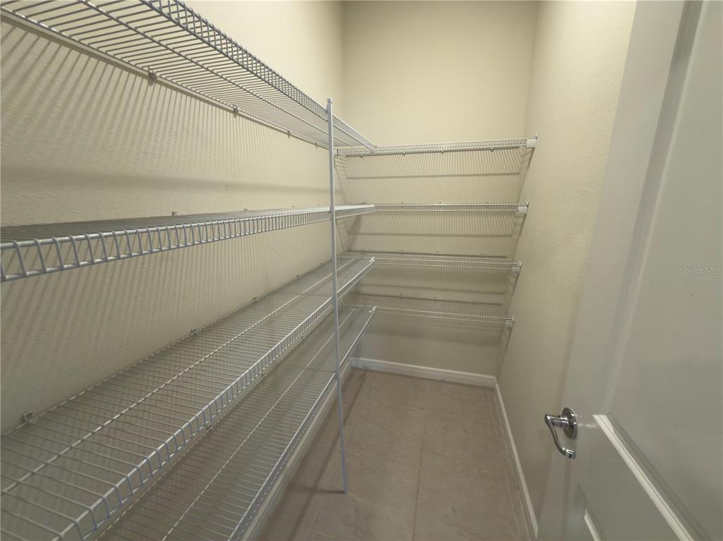 A walk-in pantry features white wire shelving units mounted on beige walls over tile flooring — 6383 TRAILBLAZE BEND, ST CLOUD, FL