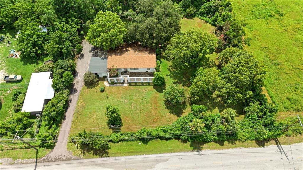 A white, flat-roofed house with a covered walkway stands in a grassy, tree-filled yard — 403 S PARSONS AVENUE, SEFFNER, FL