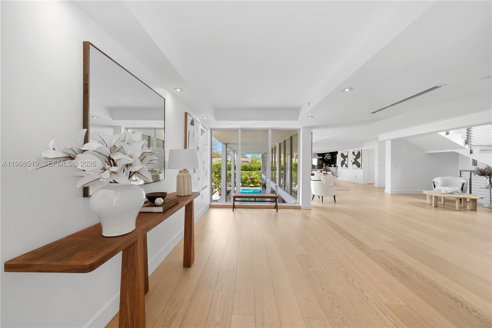 A bright, minimalist foyer features light wood flooring, a wooden console table, and floor-to-ceiling windows — 215 Palm Ave, Miami Beach FL 33139, MIAMI BEACH, FL