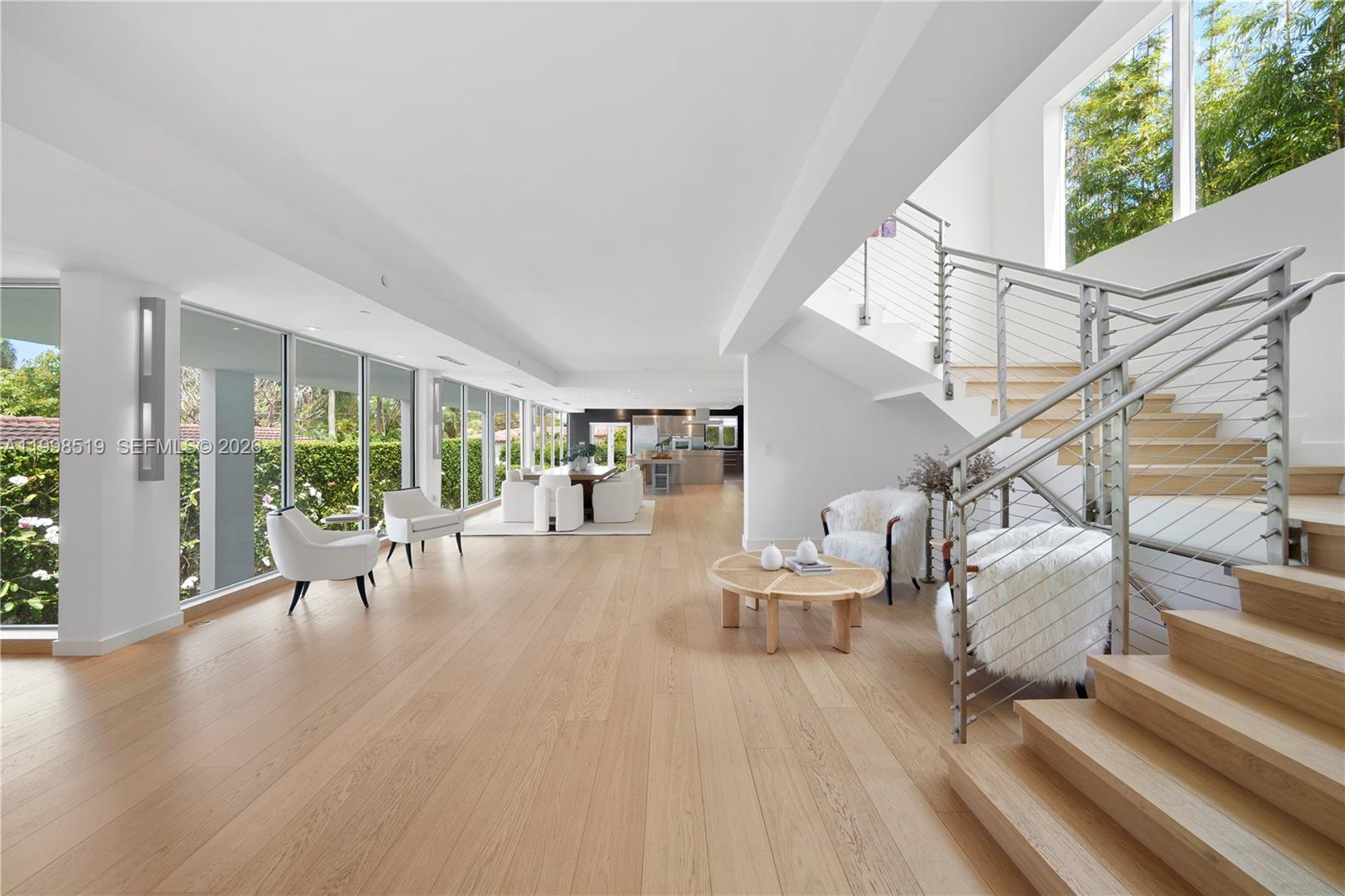 A bright, open-concept living area features light wood flooring, a staircase, and floor-to-ceiling windows — 215 Palm Ave, Miami Beach FL 33139, MIAMI BEACH, FL