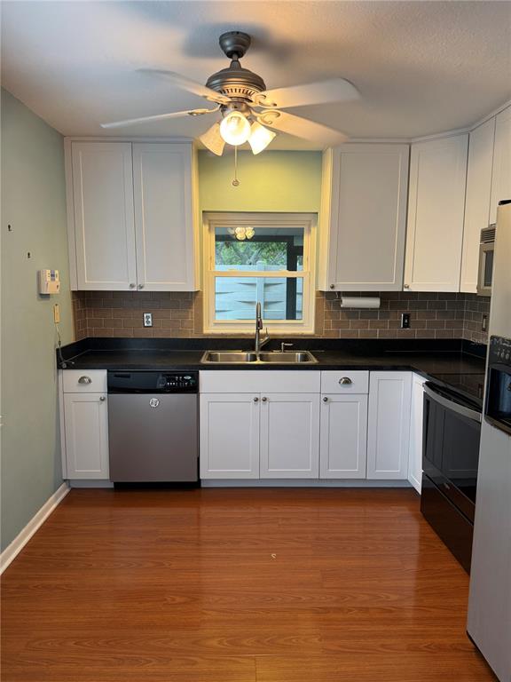 A kitchen features white cabinets, black countertops, a subway tile backsplash, and wood-look flooring — 2617 FOREST RUN COURT, CLEARWATER, FL