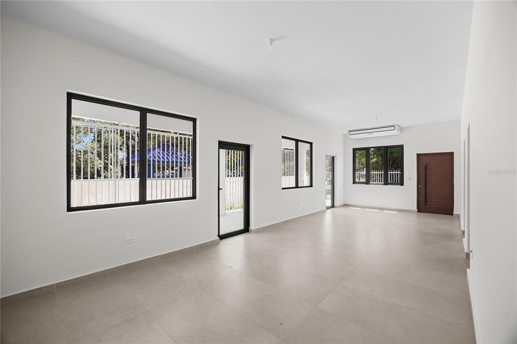 An empty room with white walls, tile flooring, black-framed windows, and a wooden door — 1207 LUCHETTI STREET, SAN JUAN, PR