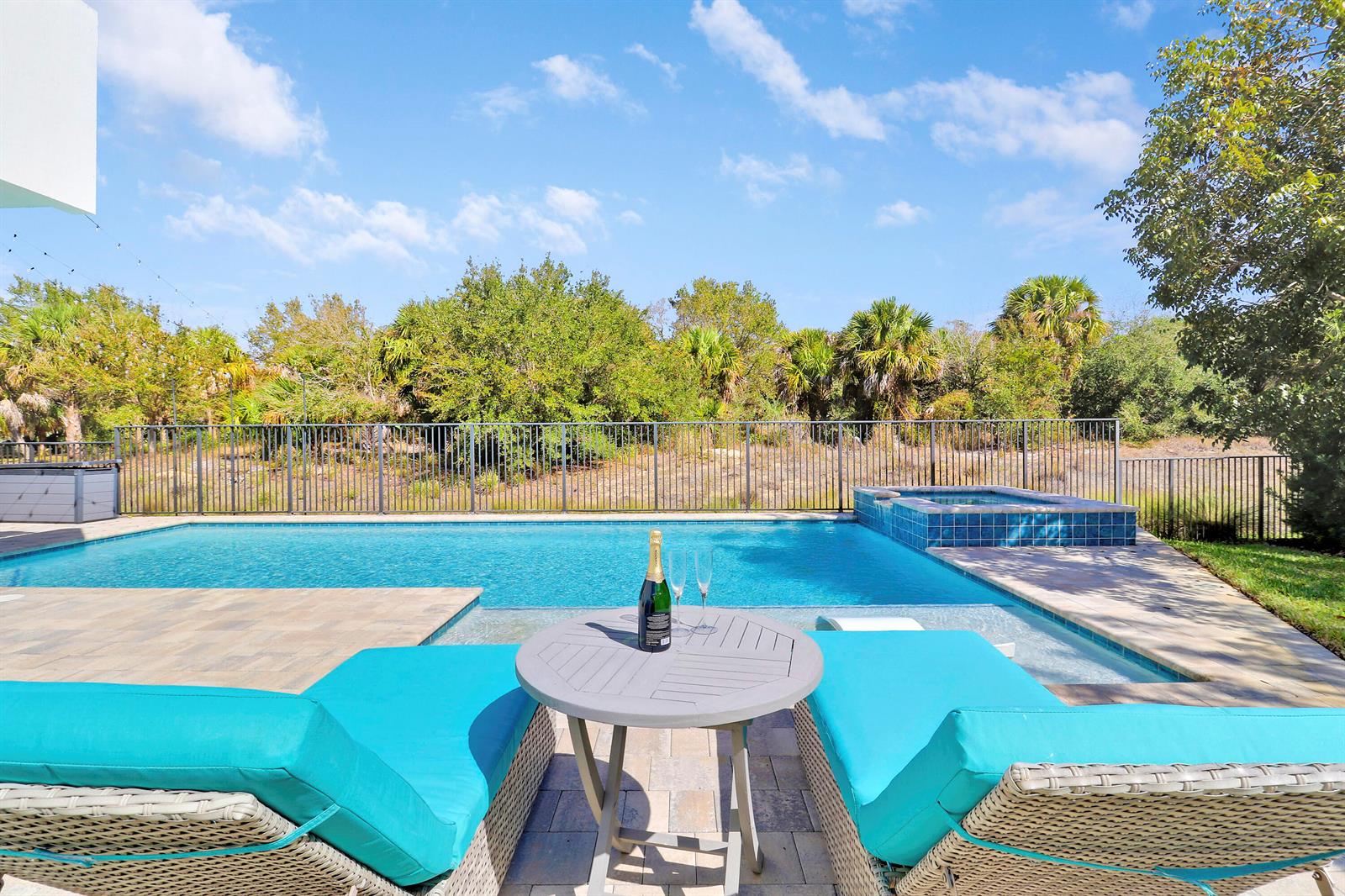 A swimming pool and hot tub are situated behind two lounge chairs and a table — 2475 NE Evinrude Circle, Jensen Beach FL 34957, JENSEN BEACH, FL
