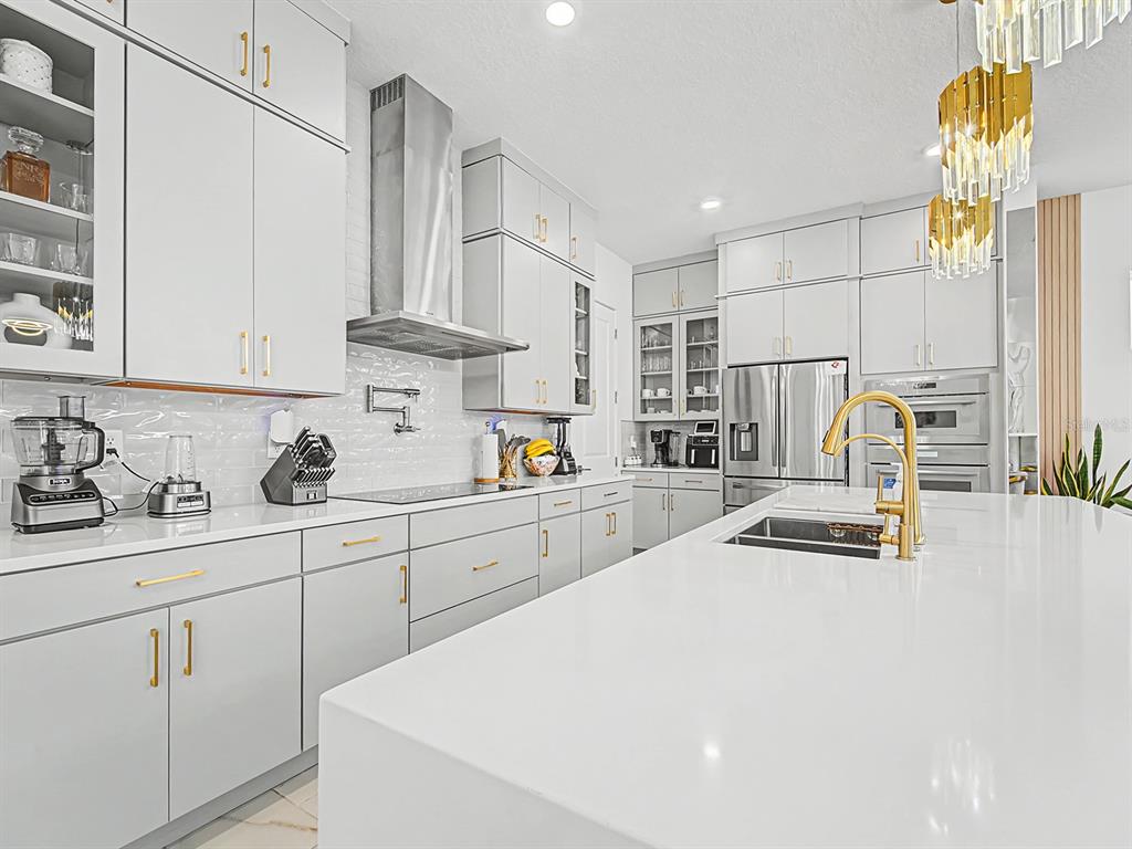 A modern kitchen features light gray cabinetry, white countertops, gold hardware, and a large island — 10537 TORCHWOOD SEA WAY, SAN ANTONIO, FL