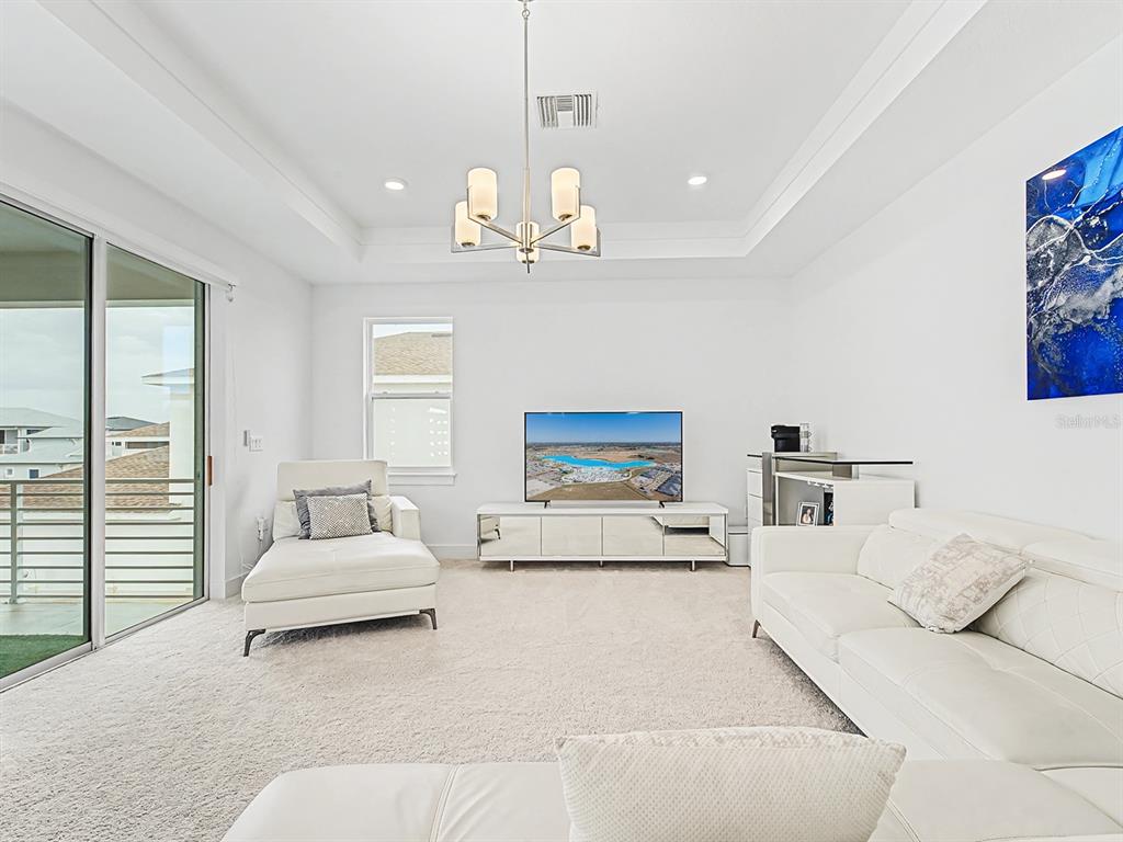A bright living room features white furniture, a tray ceiling, and a sliding glass door — 10537 TORCHWOOD SEA WAY, SAN ANTONIO, FL