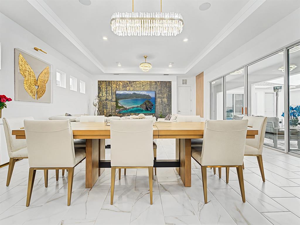 A modern dining room features a long wooden table, white chairs, and a crystal chandelier — 10537 TORCHWOOD SEA WAY, SAN ANTONIO, FL
