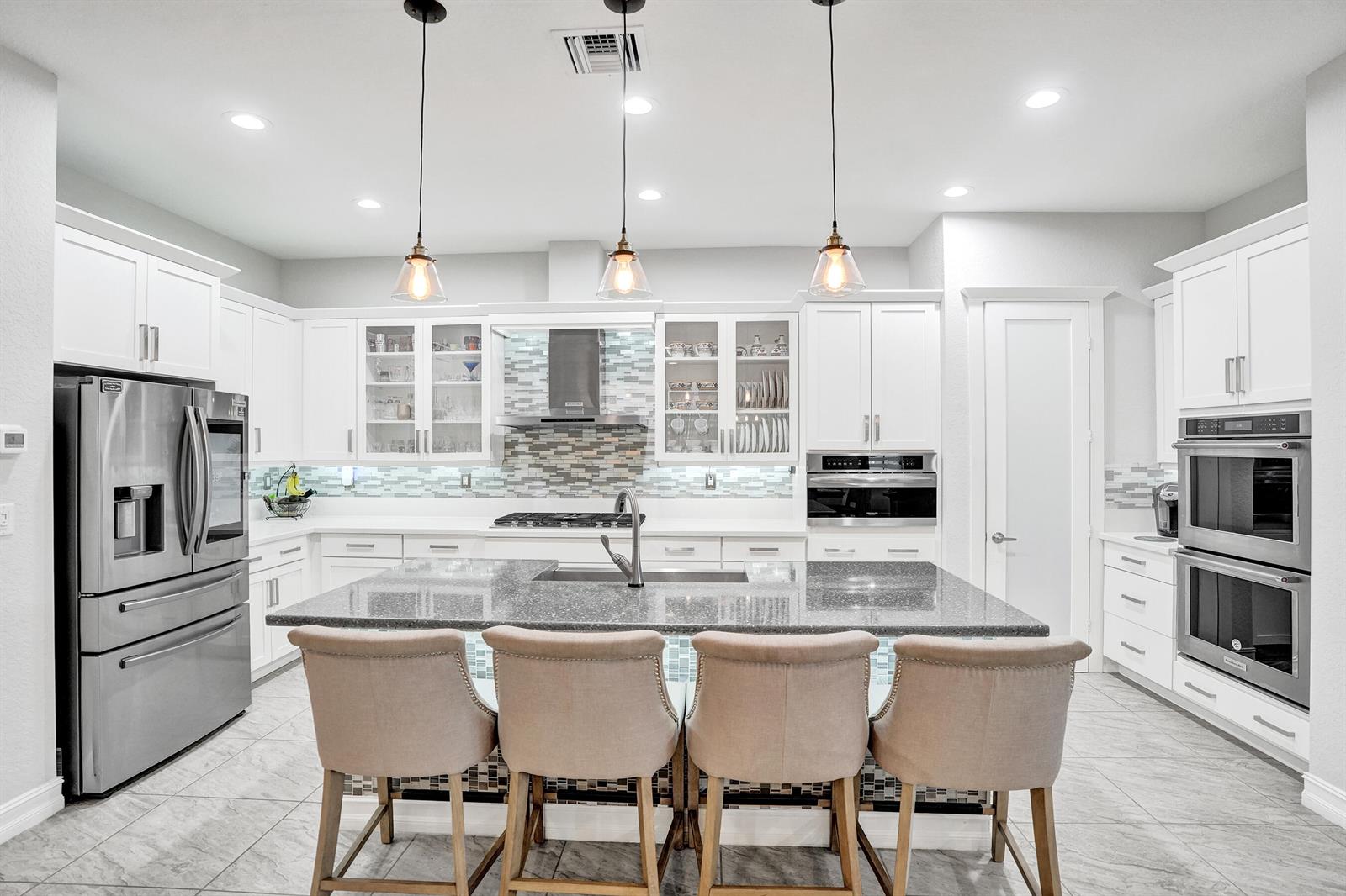 A modern kitchen features white cabinetry, a granite island with bar seating, and stainless appliances — 11405 Solstice Circle, Parkland FL 33076, PARKLAND, FL