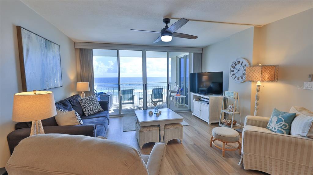 A living room features a blue sofa, striped armchair, coffee table, and sliding doors to a balcony — 4495 S ATLANTIC AVENUE UNIT 401, PONCE INLET, FL