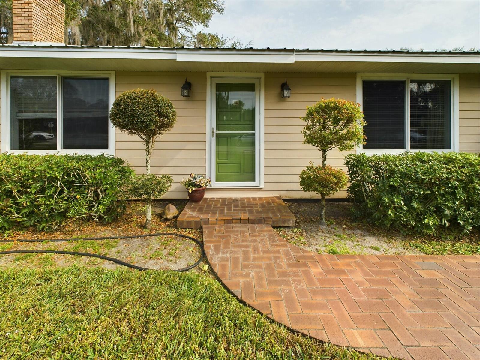 The exterior of a house features beige siding, a brick walkway, and two topiary trees — 1517 SW 7th Avenue, Okeechobee FL 34974, OKEECHOBEE, FL