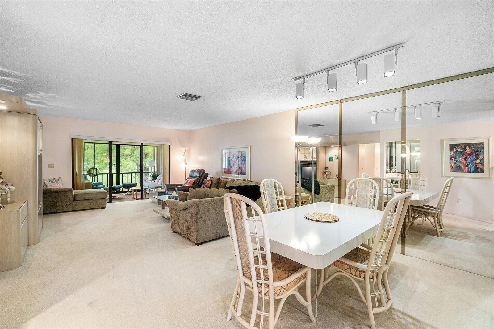 A living and dining area features beige carpeting, white furniture, and a large mirrored wall — 8320 Casa Del Lago # D, Boca Raton FL 33433, BOCA RATON, FL