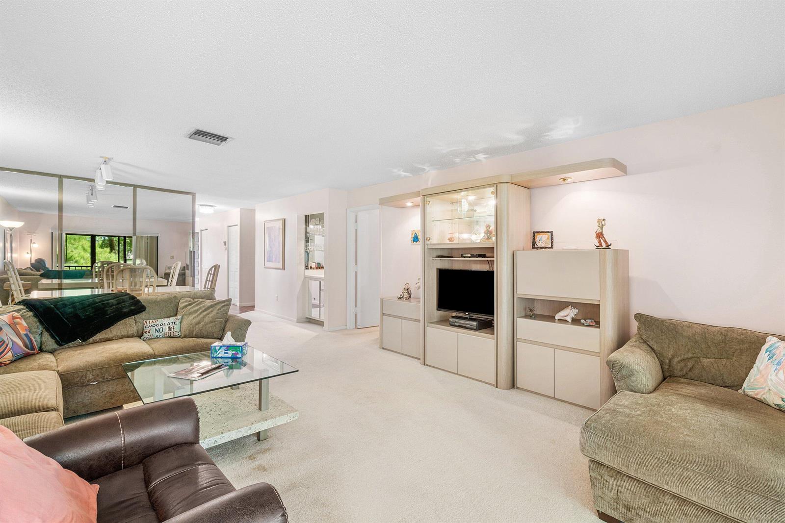 A living room features beige carpeting, a large entertainment center, and two olive-colored sofas — 8320 Casa Del Lago # D, Boca Raton FL 33433, BOCA RATON, FL