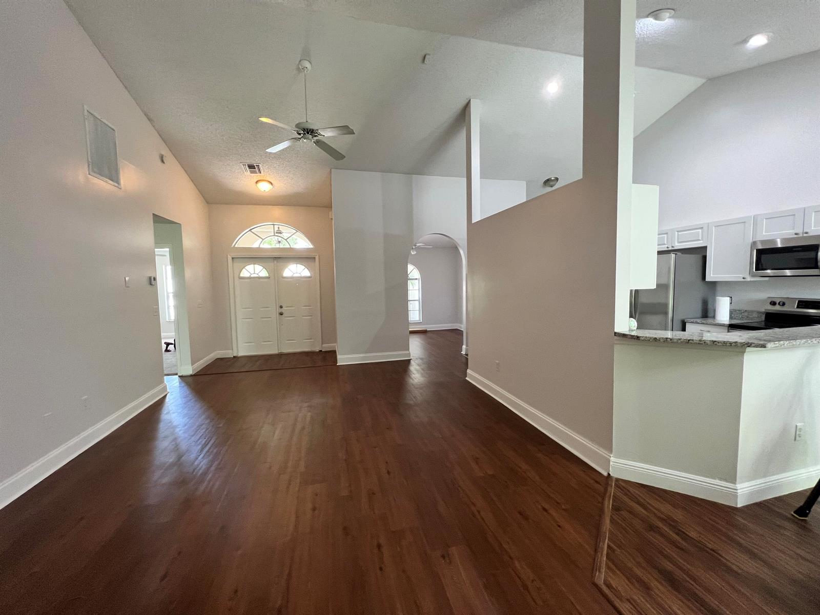 An open-concept living area features dark wood-look flooring, white walls, and a kitchen peninsula — 2485 Stonegate Drive, Wellington FL 33414, WELLINGTON, FL