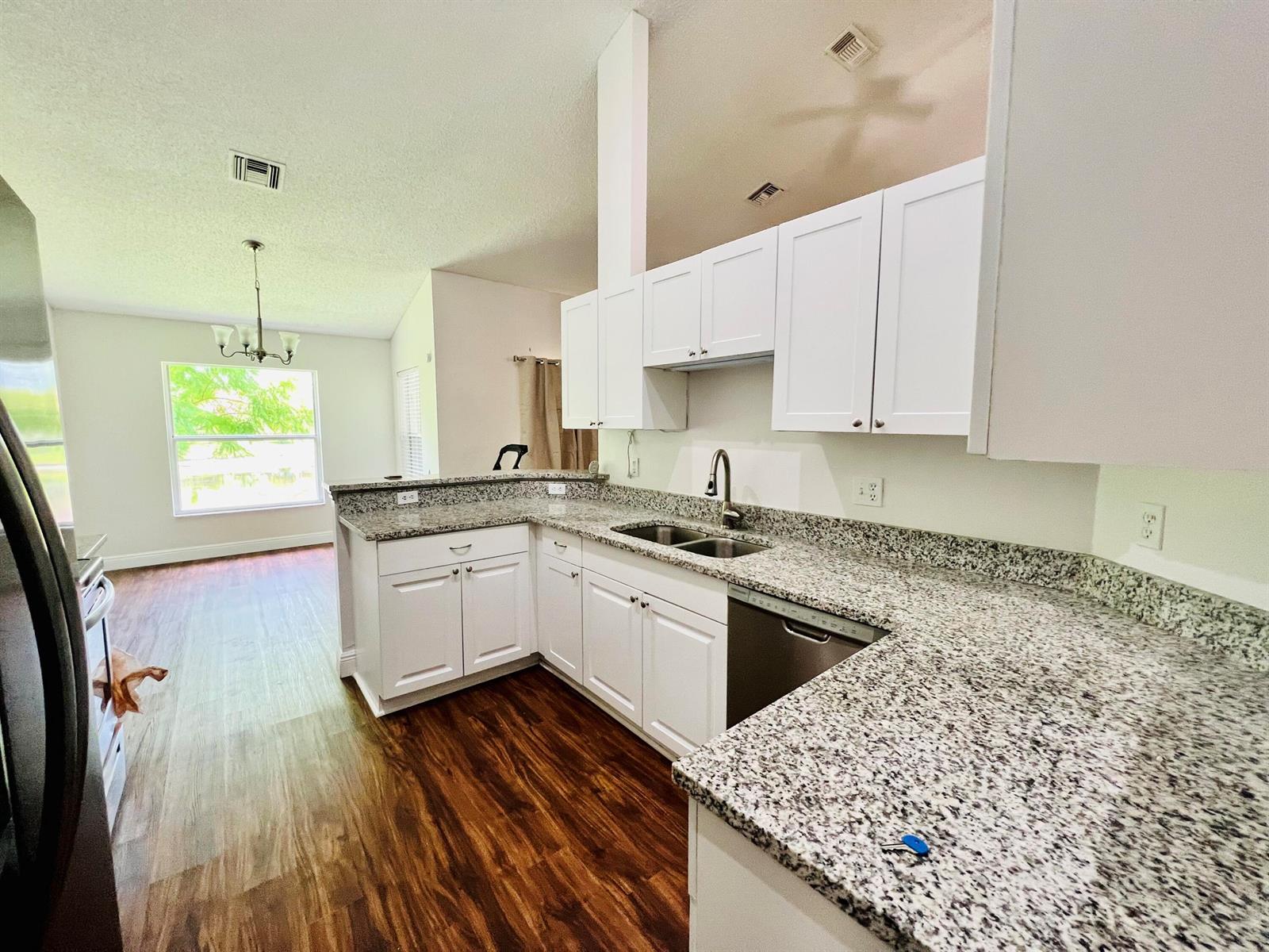 A kitchen with white cabinets, granite countertops, and stainless steel appliances overlooks a dining area — 2485 Stonegate Drive, Wellington FL 33414, WELLINGTON, FL